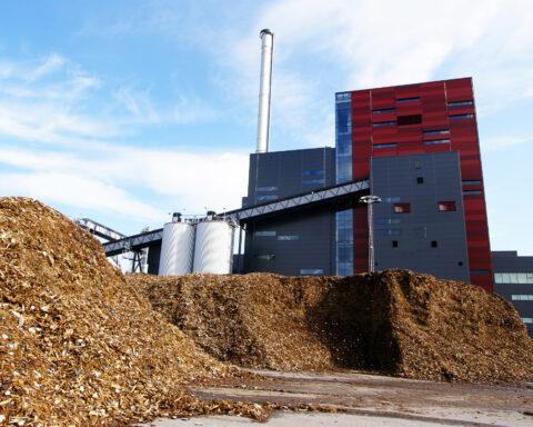 Photo of A biomass power plant with storage of wooden fuel against a blue sky.