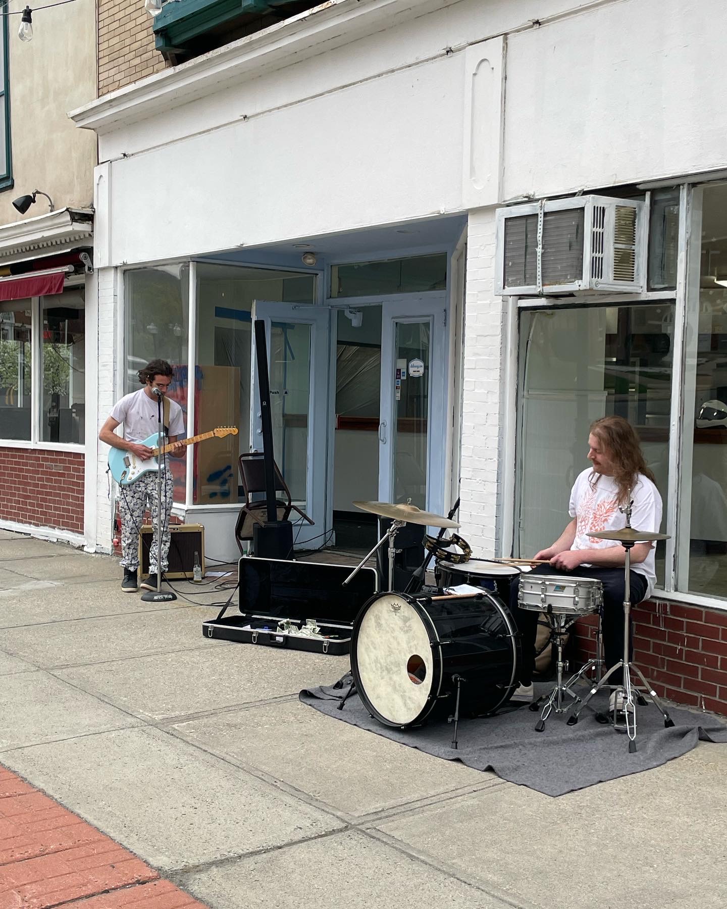 A man playing guitar and another man playing drums on a sidewalk at a block party in an urban neighborhood.