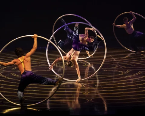 Five male acrobatic performers roll and spin in side six-foot-tall metal hoops.