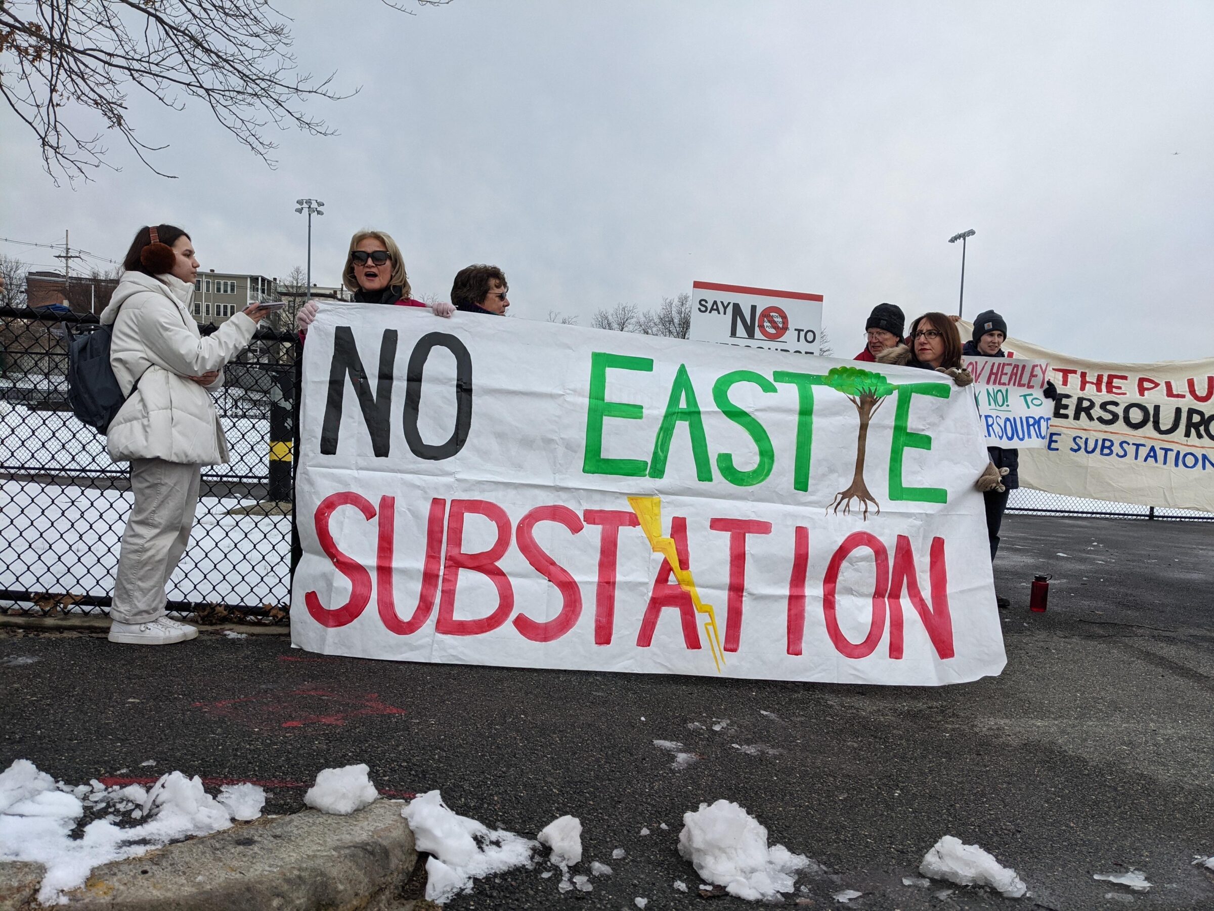An exterior shot of protesters holding up a banner that reads, "No Eastie Substation."