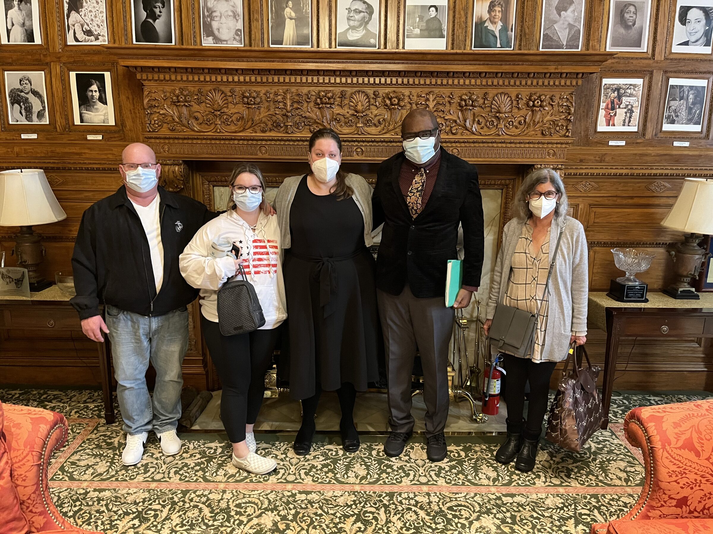 Five people, wearing surgical masks, standing in a line in front of a large fireplace.