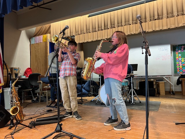 Two pre-teen music students perform on saxophone on stage.