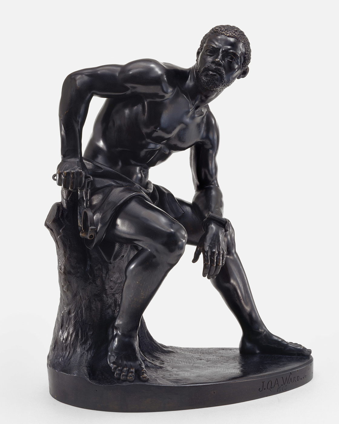 A striking black bronze sculpture titled 'The Freedman,' depicting a male figure in a moment of weary contemplation. The figure is crouched, his muscular form and defined features captured with exquisite detail. One hand rests on his knee while the other supports him on the tree stump beside, suggesting a moment of rest or reflection. The surface of the sculpture is smooth and polished, giving a lifelike quality to the man's expression and physique. There's a palpable sense of narrative and emotion in the pose and the finely rendered textures of his hair and the tree bark