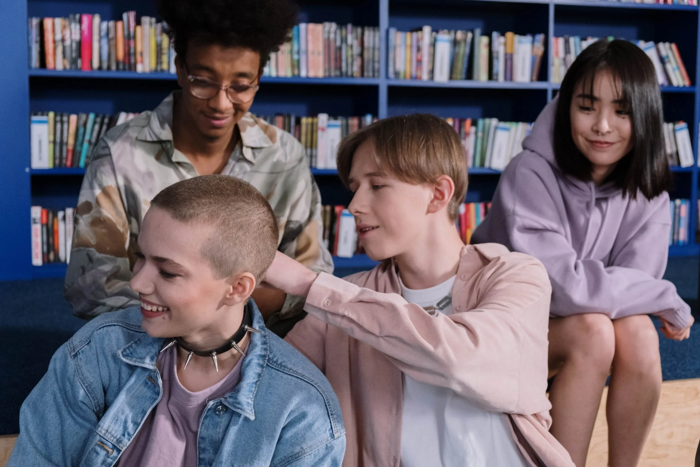 Male and female students of mixed ethnicity in a high school library joking around. One female student has a studded collar around her neck/