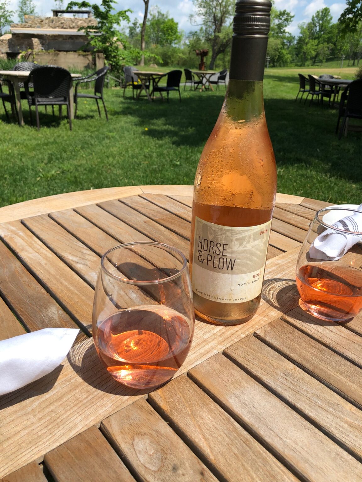 A glass and bottle of rose sit on an outdoor wooden table.