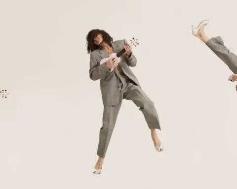 Sabina Sciubba, a woman and lead vocalist of Brazilian Girls, performing energetically with a pink ukulele. She is captured in three different dynamic poses, wearing a gray suit and white heels, against a plain background. Sciubba is known for her genre-bending, multilingual music and has received critical acclaim and a Grammy nomination.