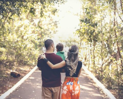 photo of family walking in the park along a paved trail through a wooded area with the sun shining down through the leaves overhead